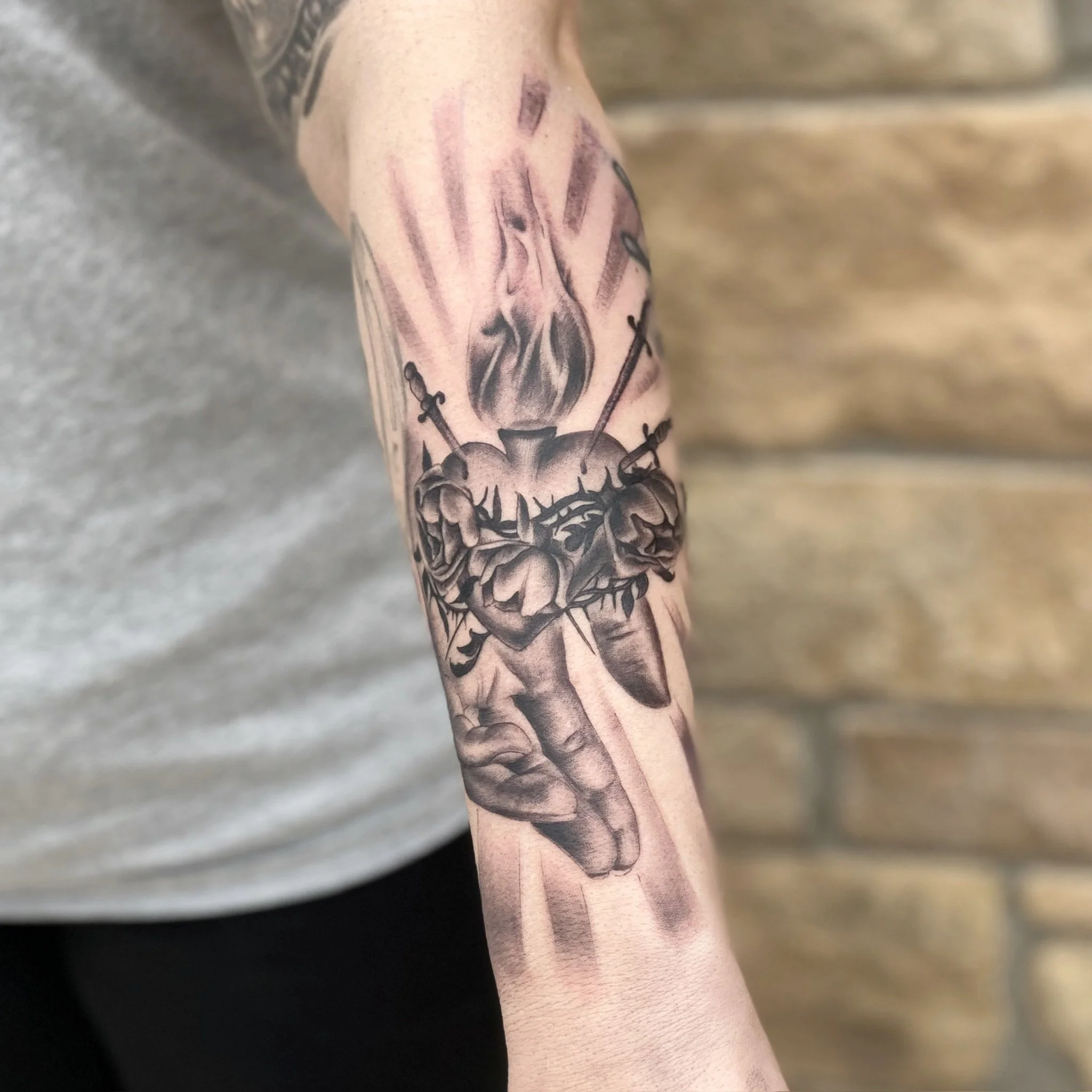 Black and gray tattoo of a realistic human heart with a rose growing from it, with swords pierced through the heart and flames above.