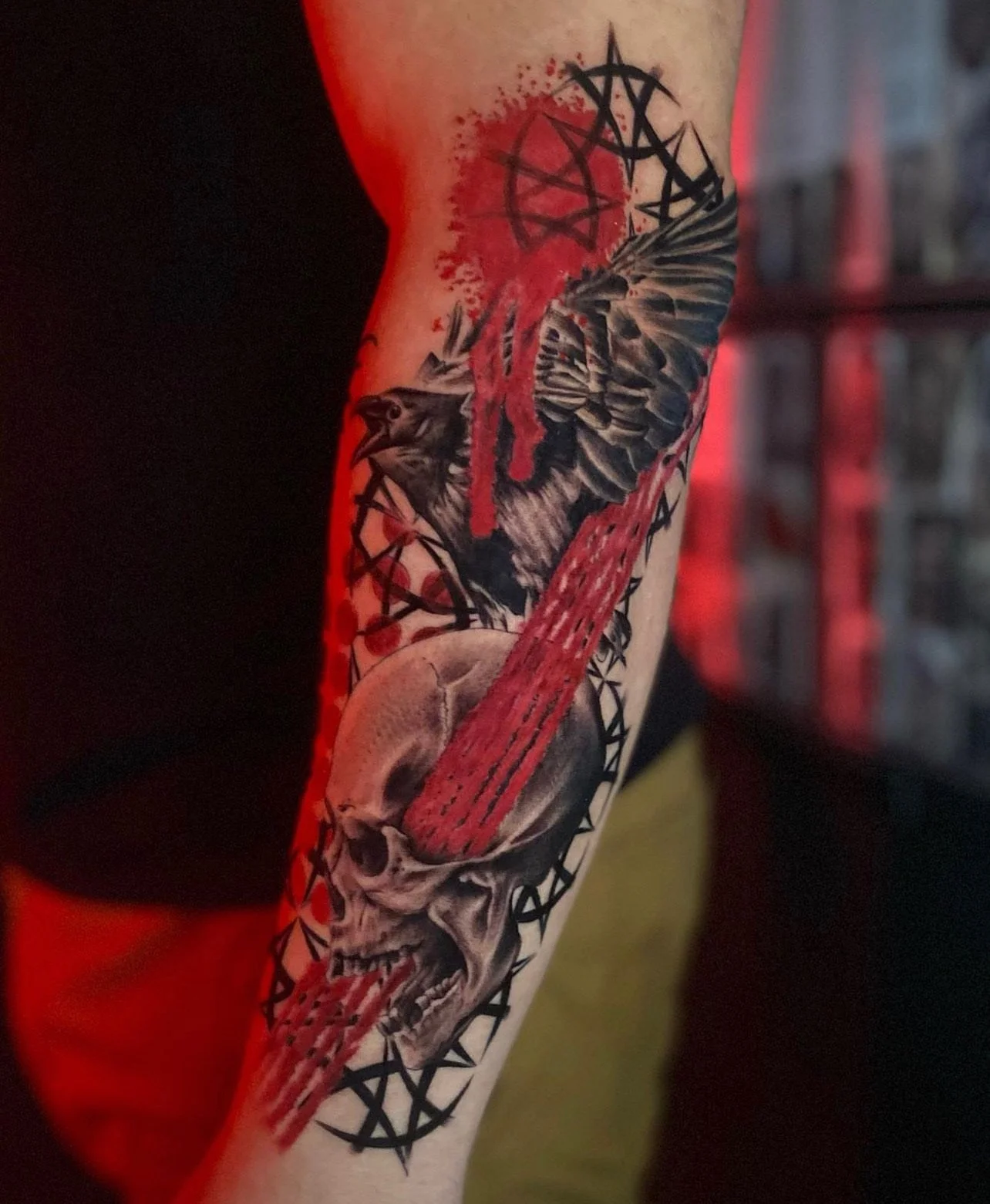 Tattoo of a skull with a knife through it, a raven, and pentagrams with red and black ink.