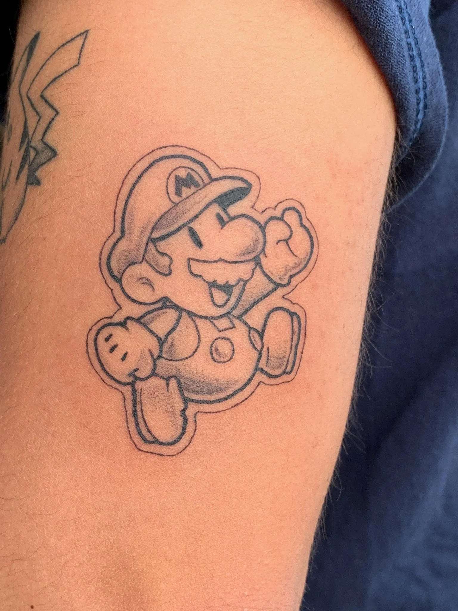 Black line drawing of Mario, a popular video game character, smiling and waving, with a rounded outline around the figure.