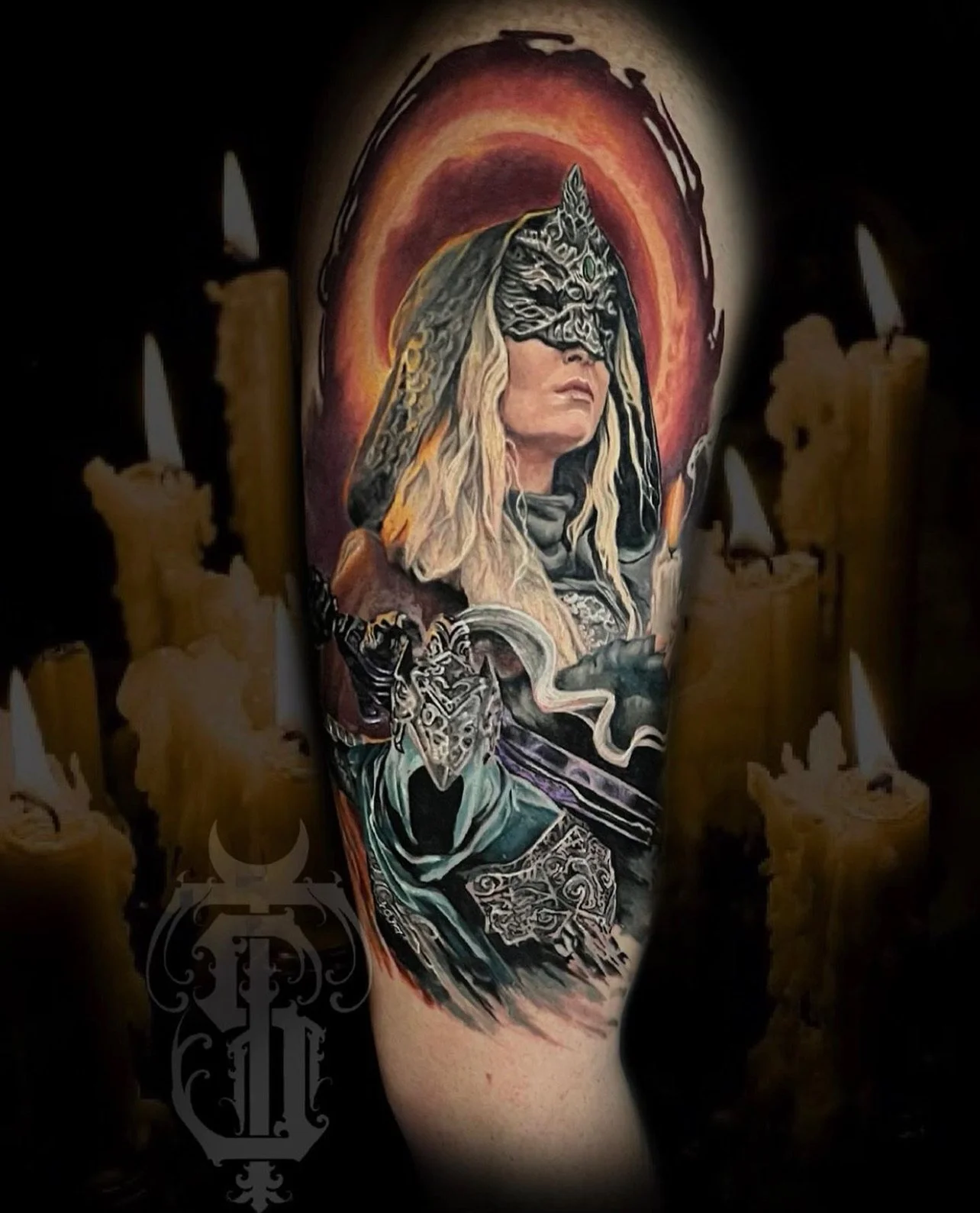 Tattoo of a woman with long blonde hair, wearing a mask and armor, holding a sword, with a halo-like background and surrounded by candles.