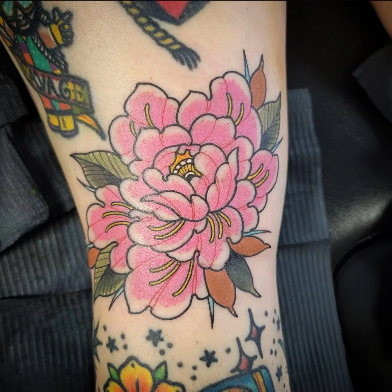 a pink peony, in neo-traditional tattoo style with green brown, and yellow leaves on someone's leg 