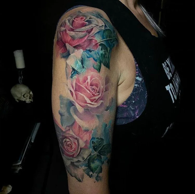 Colorful watercolor-style tattoo of pink roses on a person's upper arm and shoulder.
