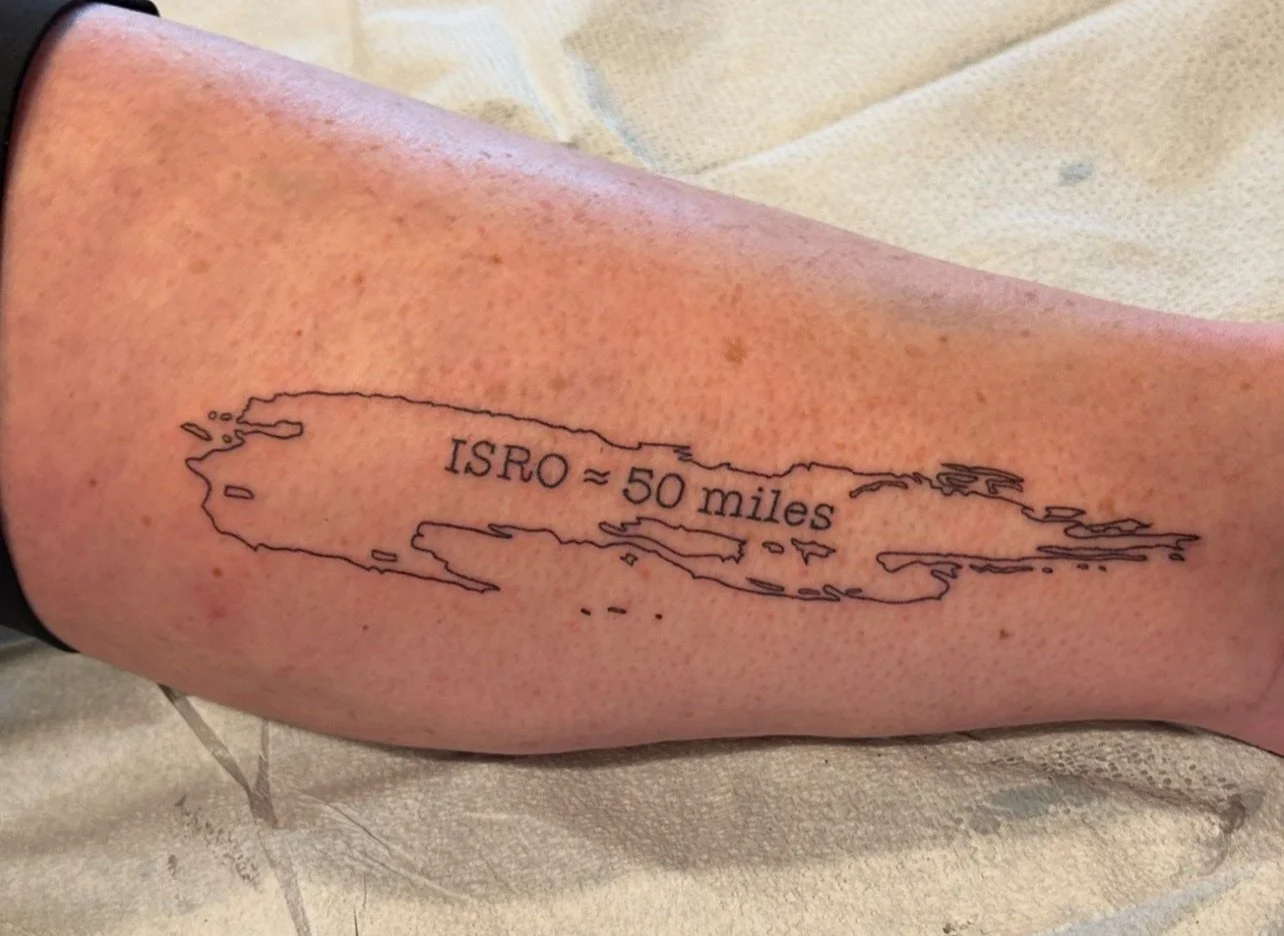 Tattoo of a map outline with the text 'ISRO ≈ 50 miles' on a person's leg.