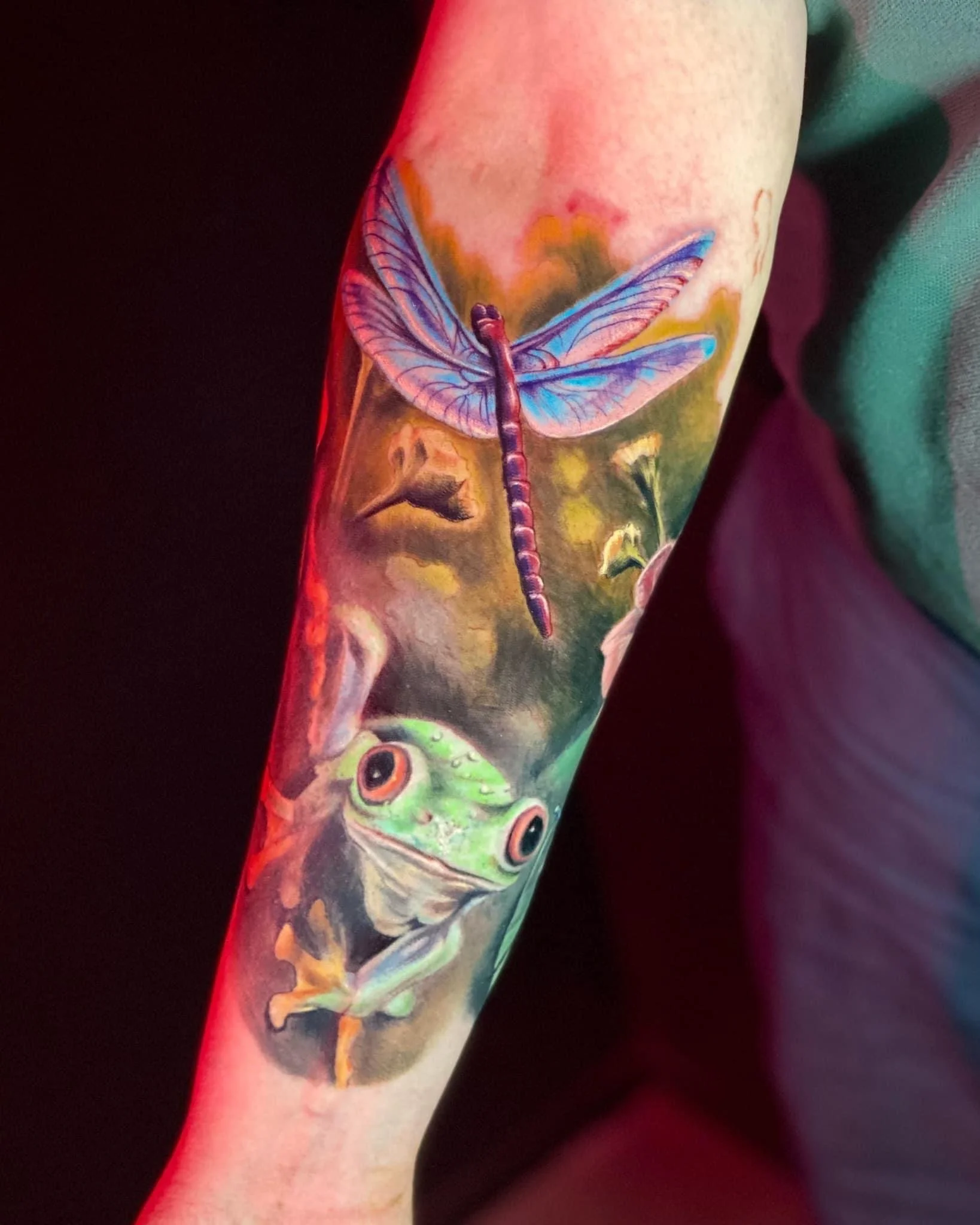 Colorful tattoo of a dragonfly and a frog on a person's arm.