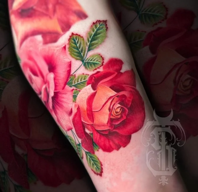 A close-up of a tattoo featuring red and pink roses with green leaves on a person's arm.