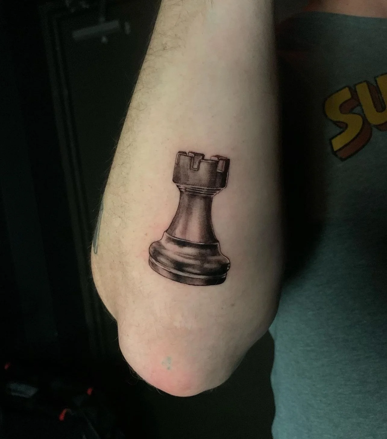 Tattoo of a black king chess piece on a person's upper arm.