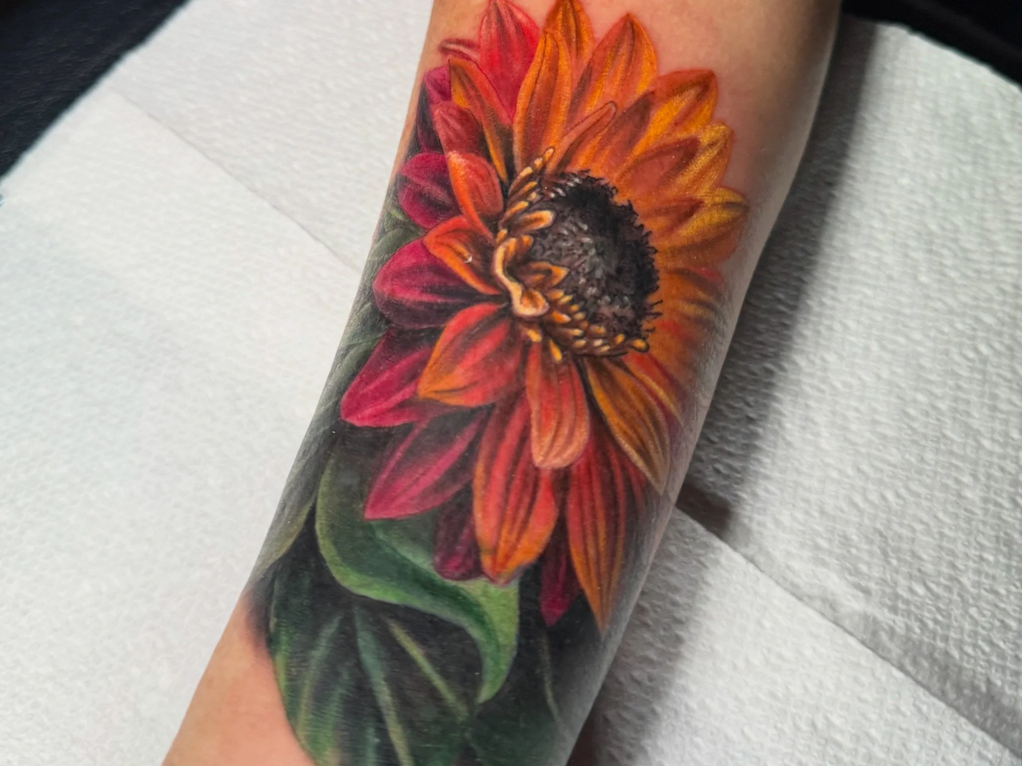 Colorful realistic sunflower tattoo on a person's arm.