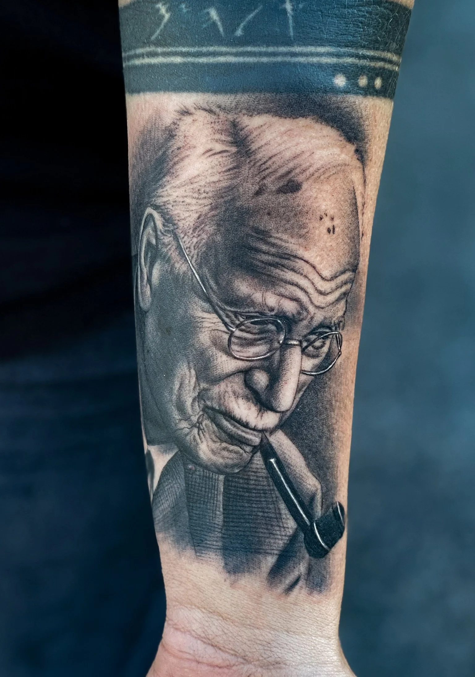 Black and grey realistic tattoo of Albert Einstein's portrait on a person's forearm, with detailed facial features, glasses, and a pipe in his mouth.