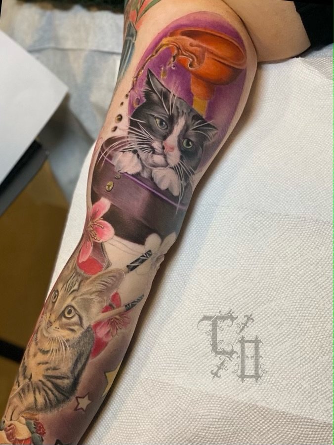 A detailed colorful tattoo sleeve of two cats, flowers, and a pumpkin, on a person's arm.