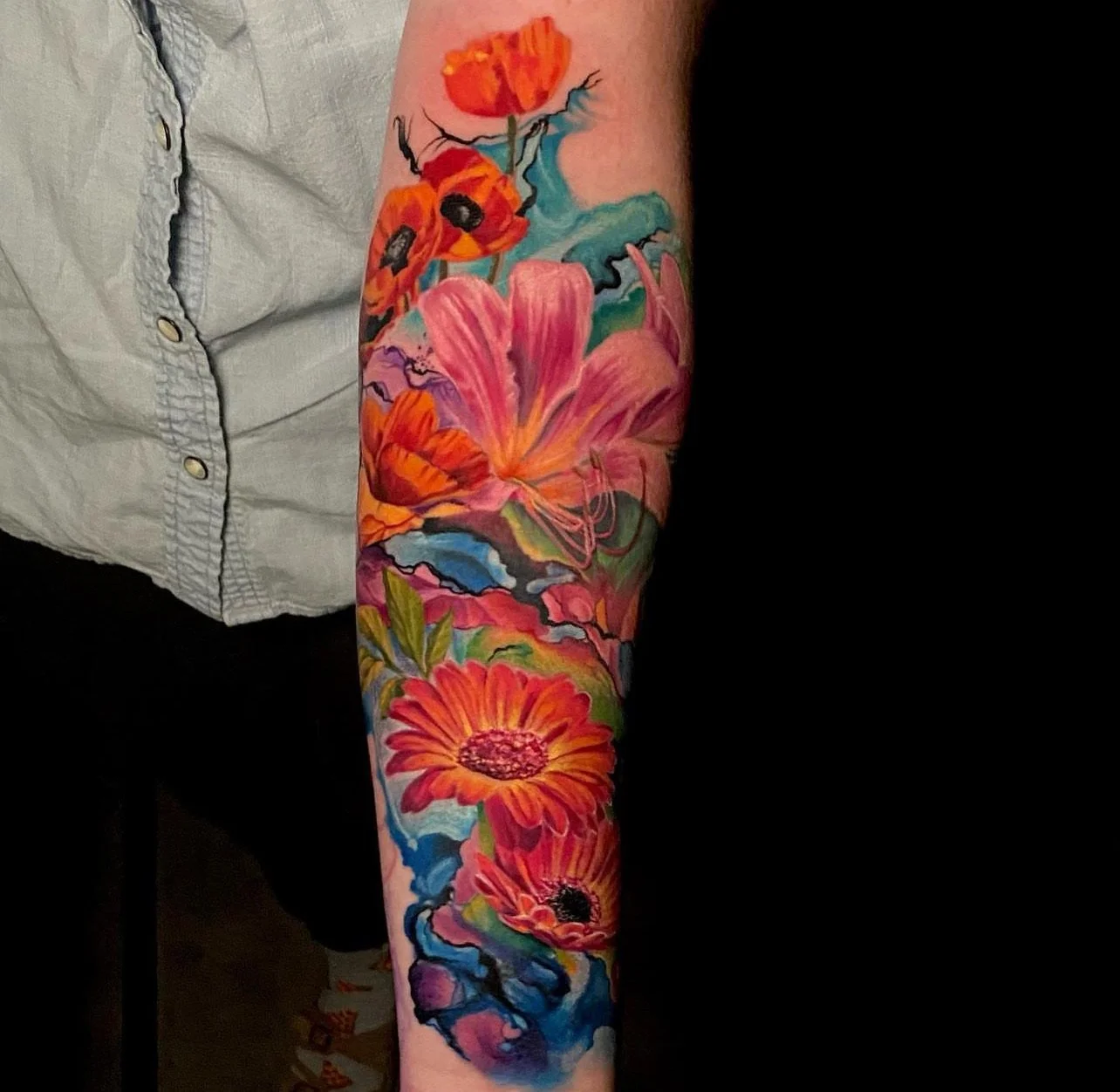 Colorful tattoo sleeve featuring flowers, including lilies and daisies, with vibrant blues, pinks, reds, and oranges.
