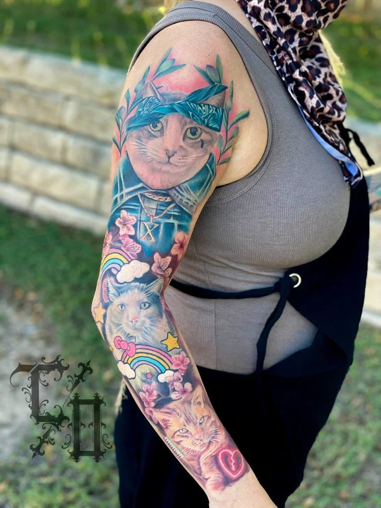 Colorful tattoo sleeve featuring three realistic cat portraits, rainbows, clouds, pink flowers, and a heart on a person's arm.