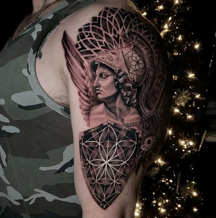 Tattoo of a woman wearing a helmet with a feathered crest, and armor with geometric patterns, on a person's arm.