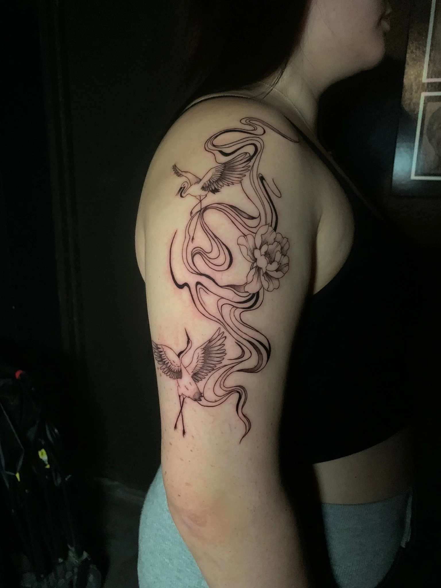 Tattoo of two flying cranes, a flower, and flowing lines on a woman's upper arm and shoulder.