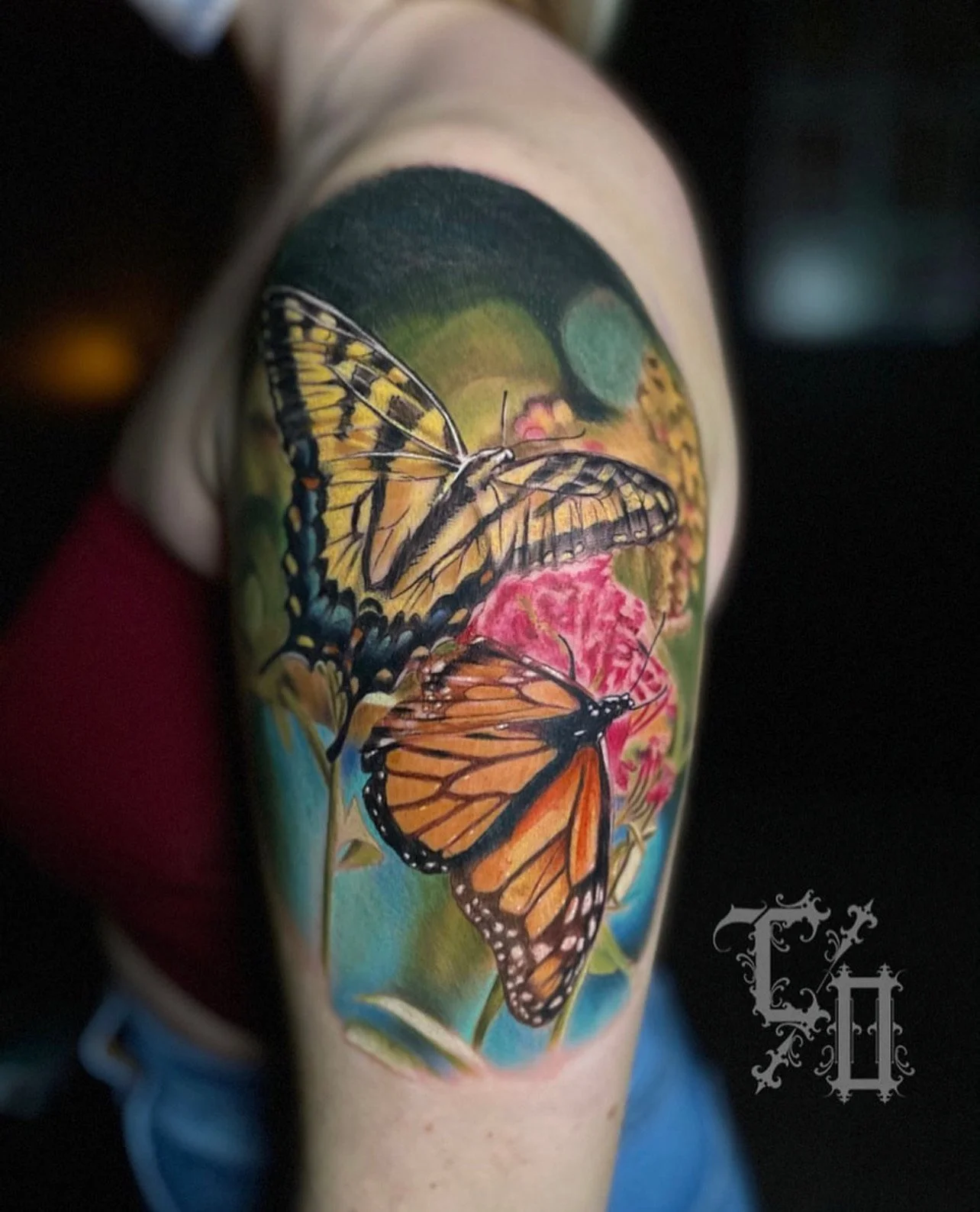 Colorful tattoo of yellow and black butterflies with orange and black butterflies on a person's upper arm, featuring pink flowers and green background.