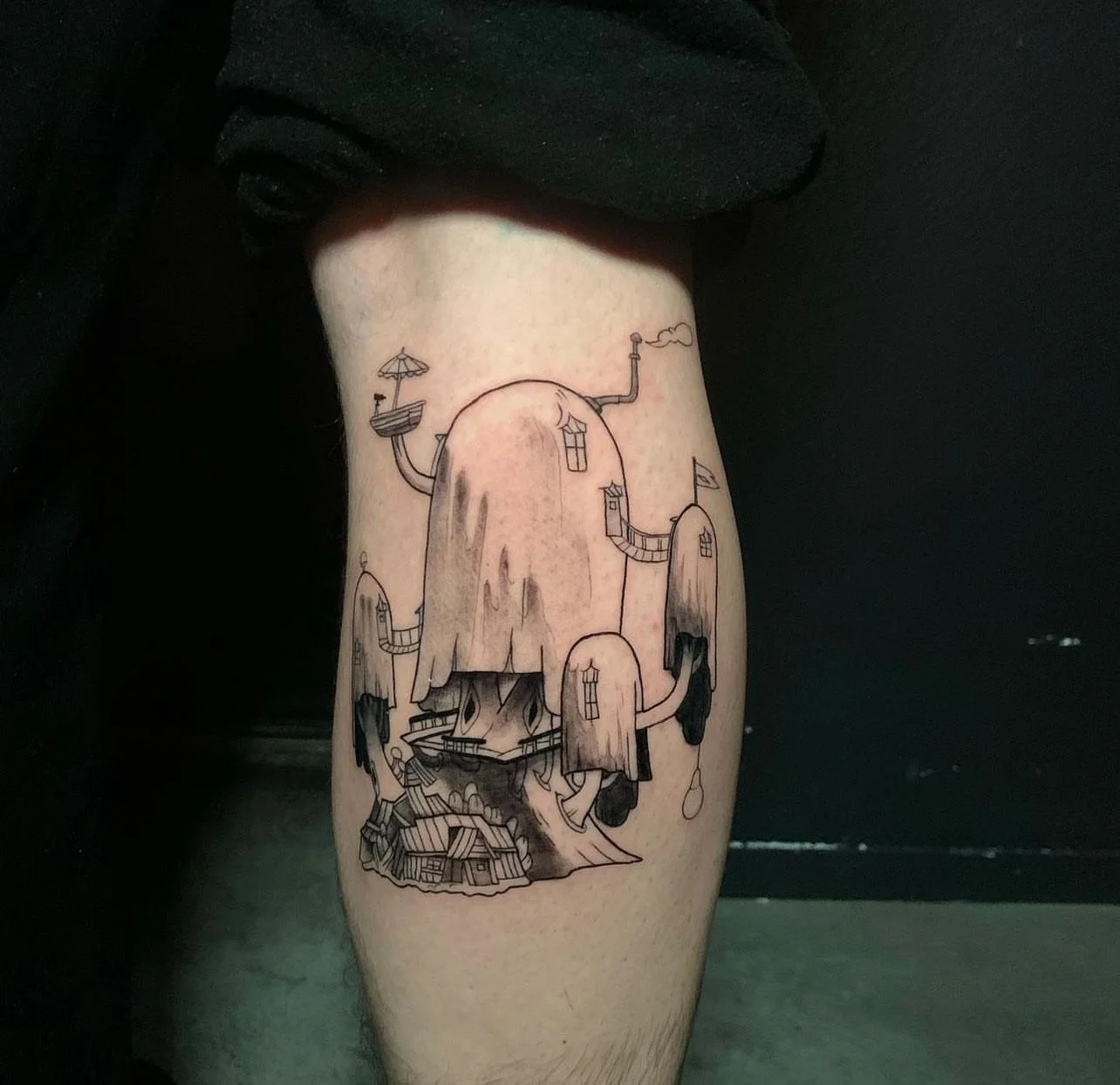 Black and gray tattoo of a whimsical house built on a large hill with multiple smaller houses connected by pathways, with smoke coming from a chimney at the top.