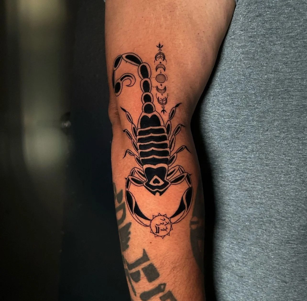 Black outline tattoo of a scorpion with decorative elements on the forearm.