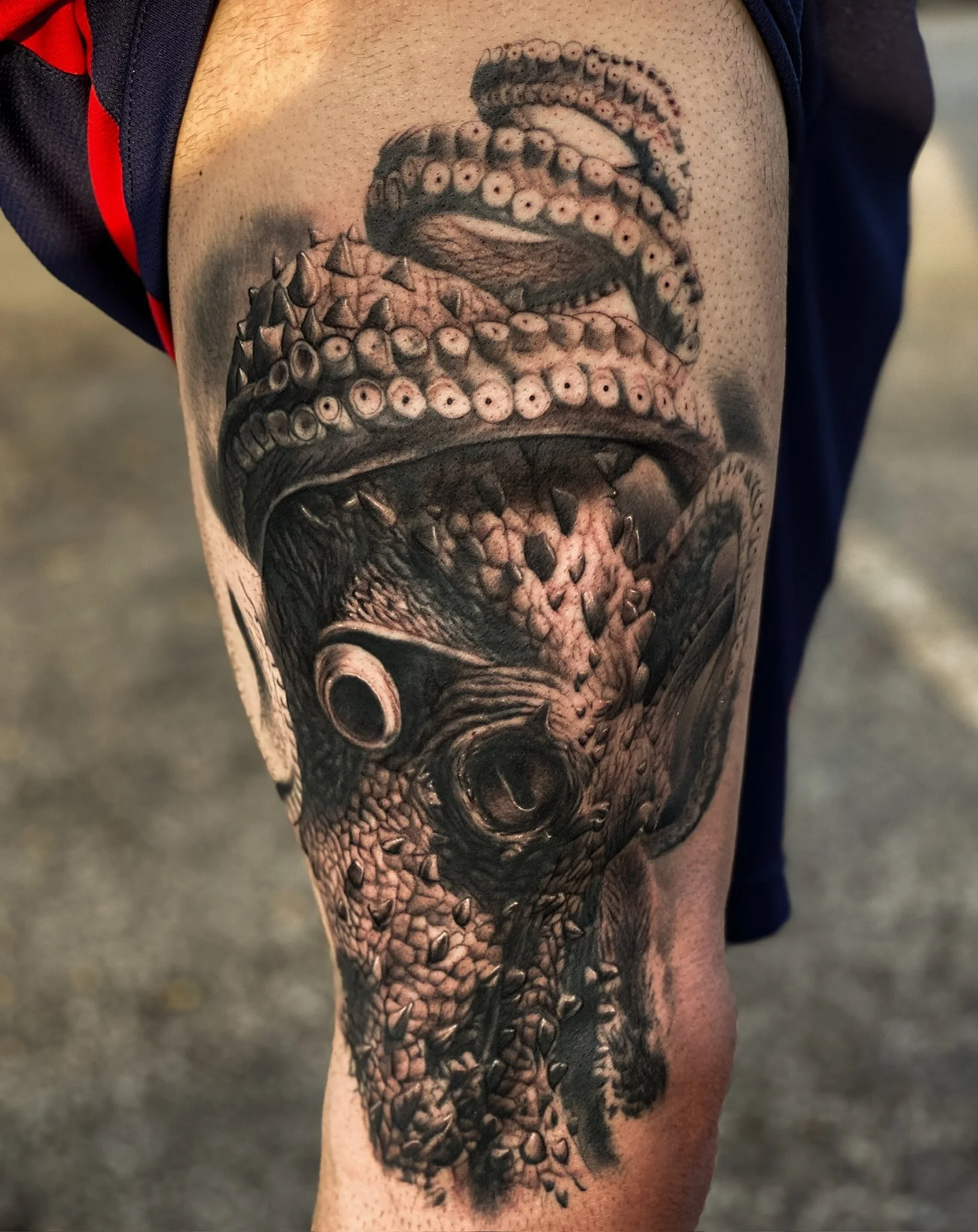 Black and gray tattoo of a detailed, menacing octopus with its tentacles wrapping around a dog's face, showing sharp teeth and textured skin.