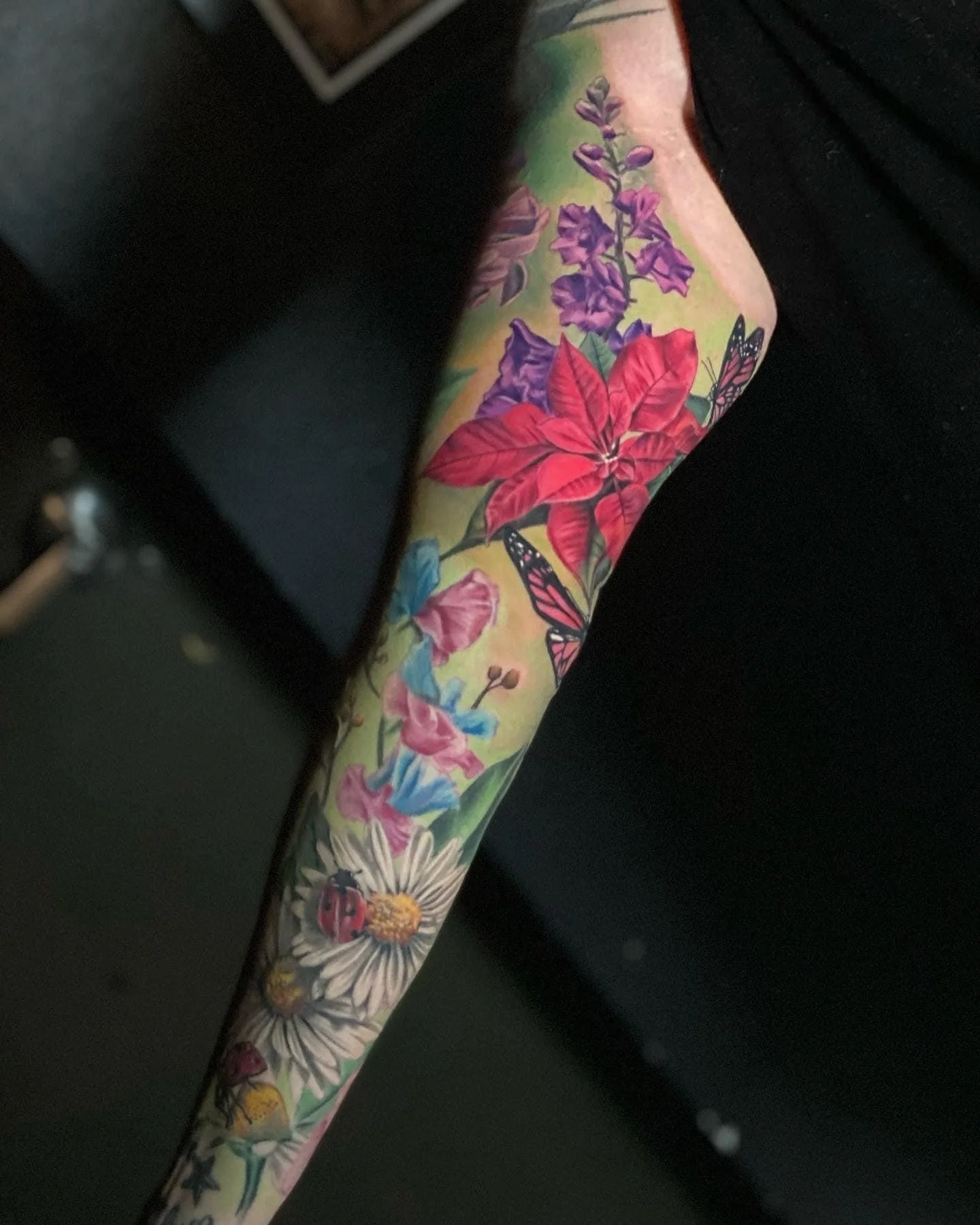 Colorful tattoo sleeve featuring flowers, insects, and butterflies on a person's arm.