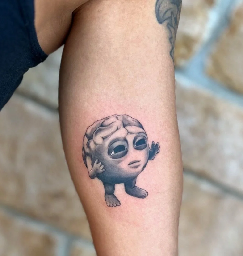 Tattoo of a small, cartoonish brain with a face, arms, and legs, appearing tired or sad.