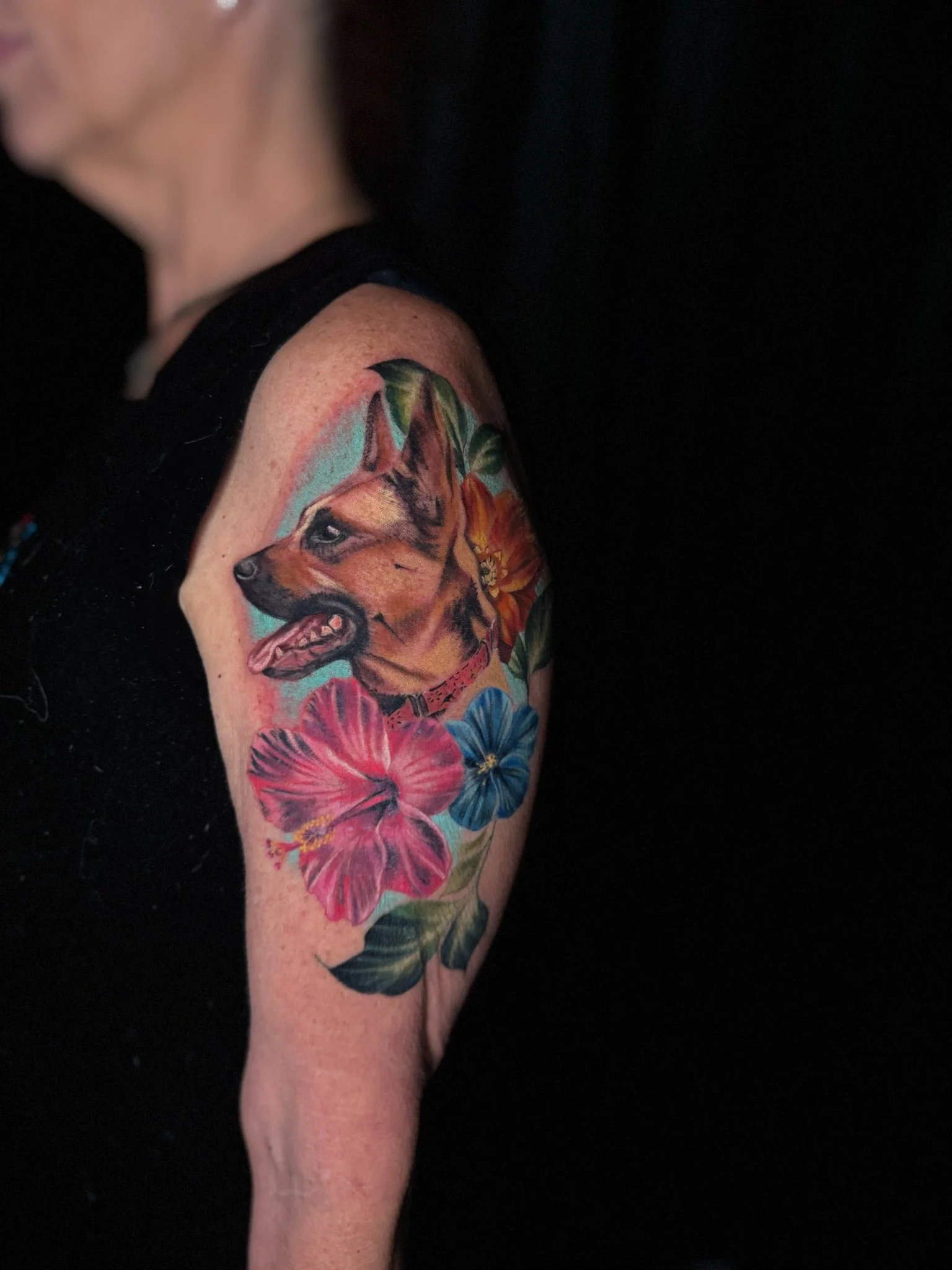 Tattoo of a dog’s face surrounded by colorful flowers on a person's upper arm.