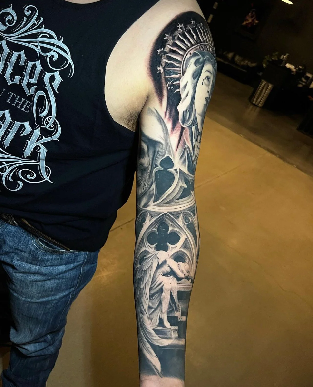 Black and gray tattoo sleeve featuring religious and gothic elements, including a woman with a halo, skulls, and angelic figures.