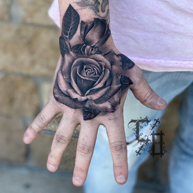 A tattoo of a detailed black and gray rose on the person's hand, extending onto the wrist and forearm.