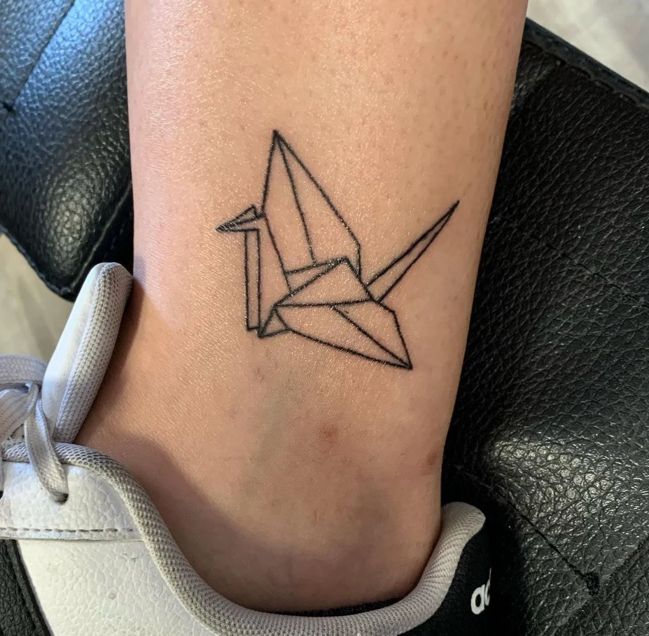 Line art tattoo of an origami crane on a person's upper thigh.