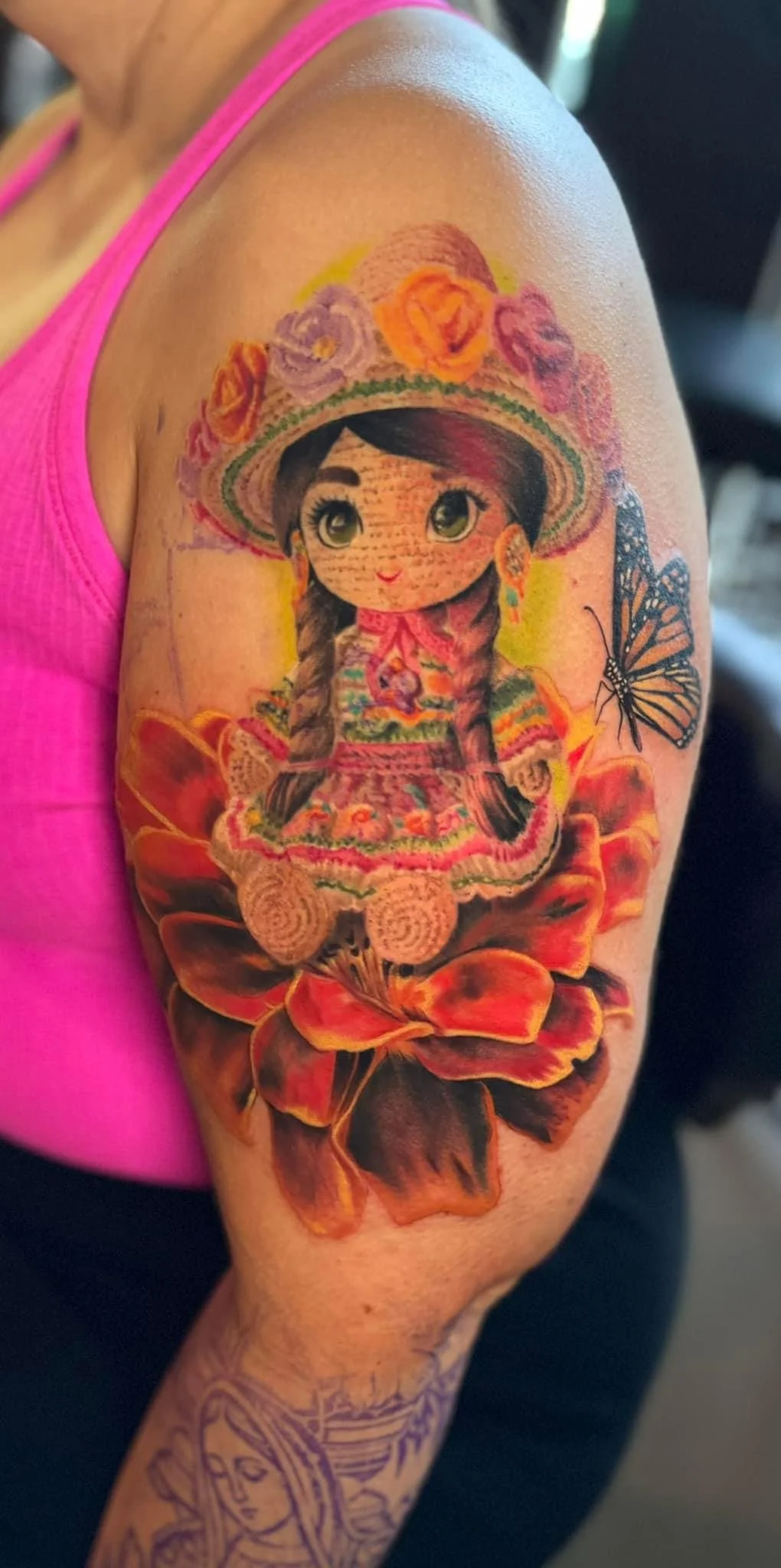 Tattoo of a girl with large eyes wearing a traditional dress and hat, surrounded by flowers and a butterfly, on the upper arm.