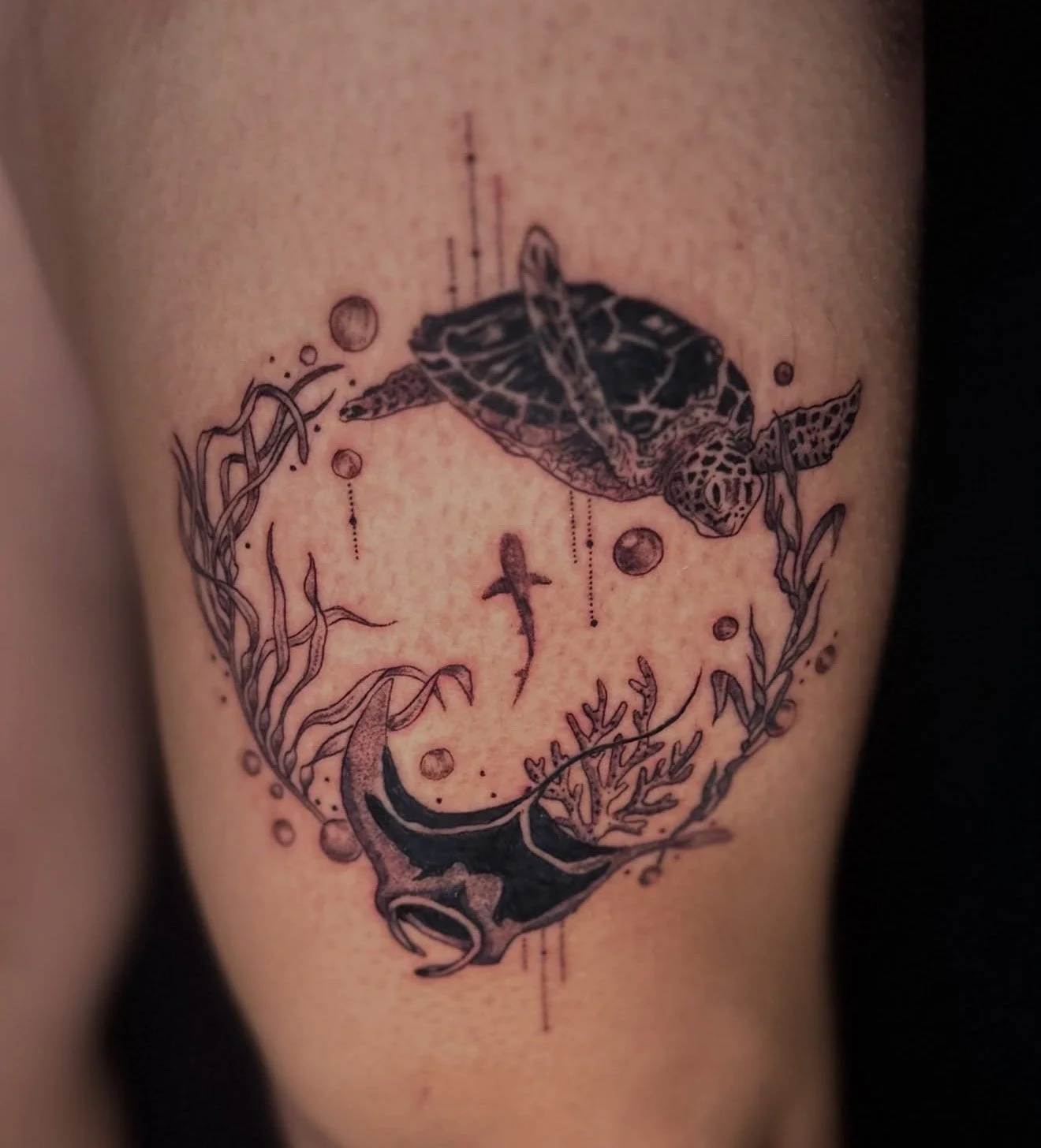 Tattoo of a turtle swimming among seaweed, a fish, and coral, with abstract lines and bubbles surrounding it.