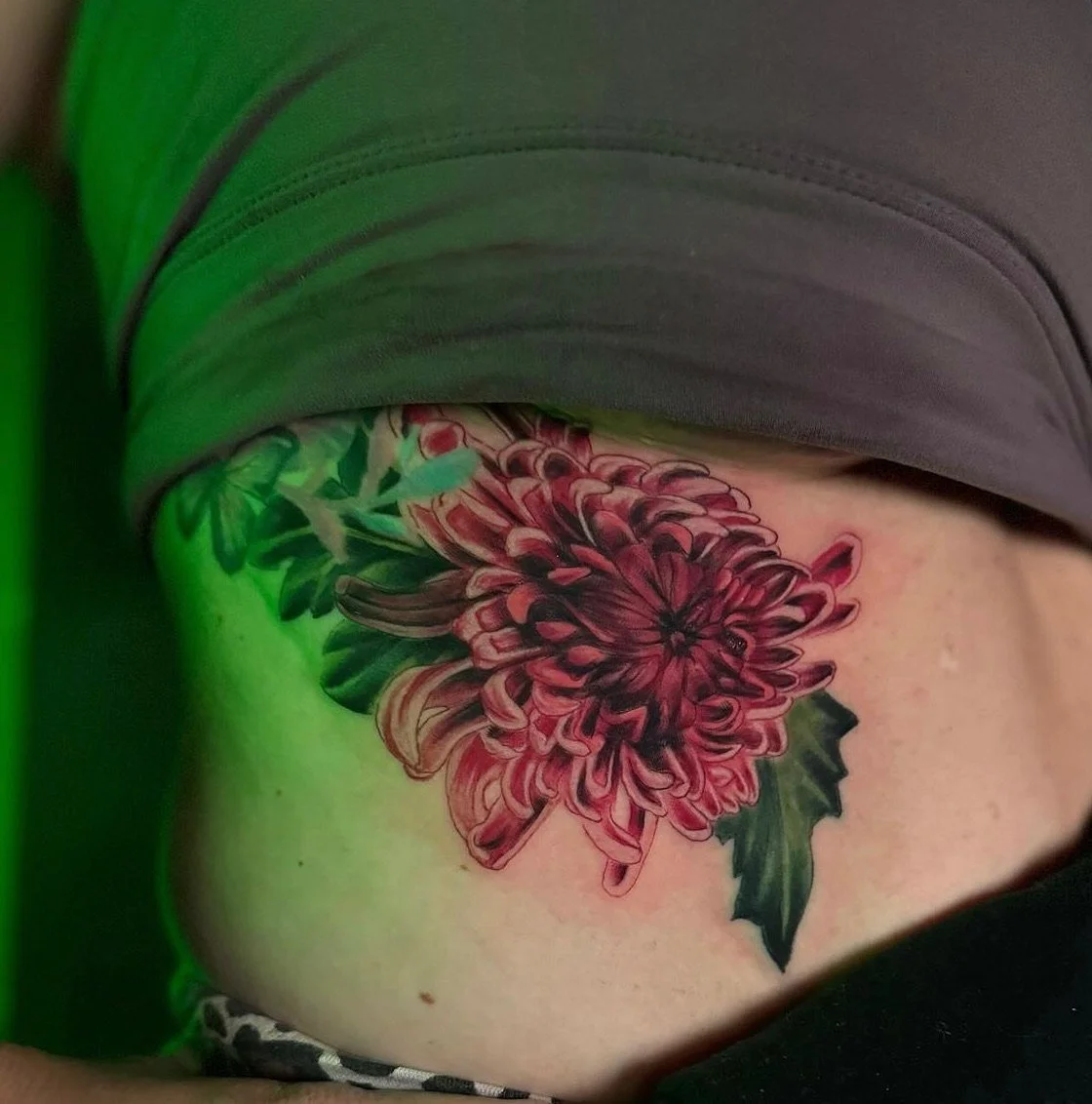 Colorful floral tattoo on person's side, featuring a large red and pink flower with green leaves.