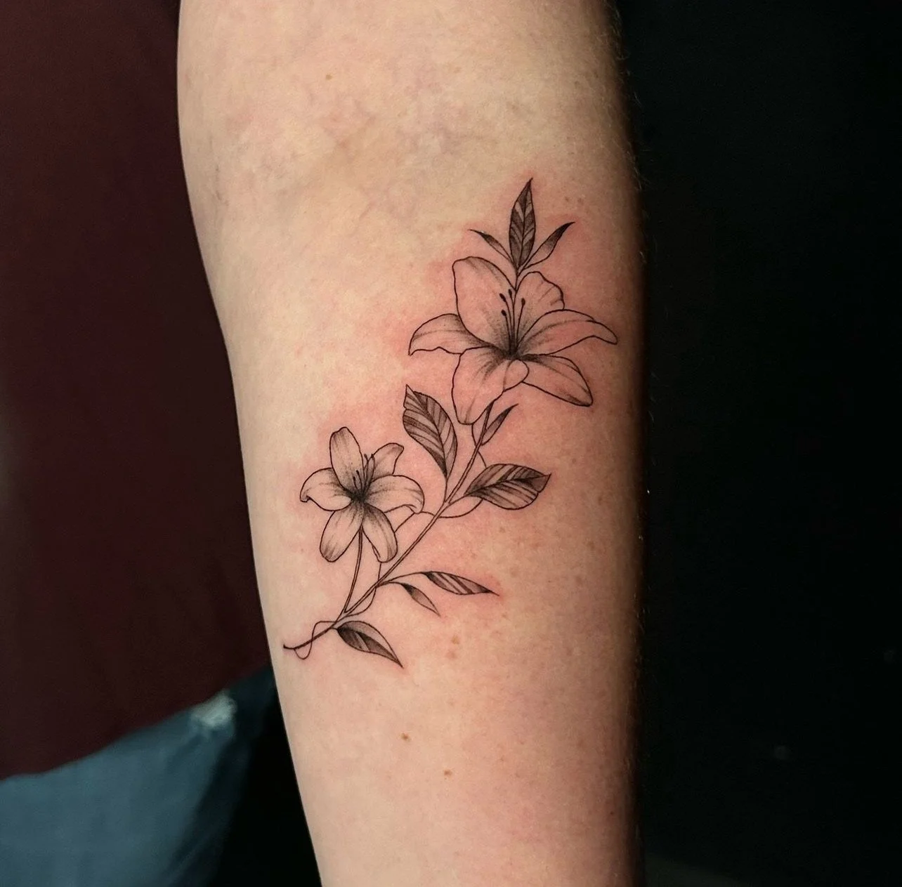 Black and gray floral tattoo of two lilies with leaves on a person's arm.