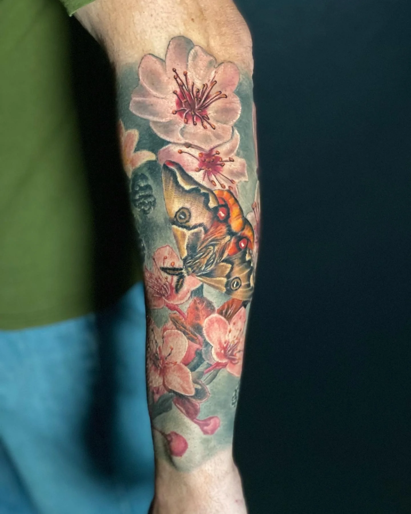 Colorful tattoo of pink cherry blossoms and a butterfly on the person's arm.