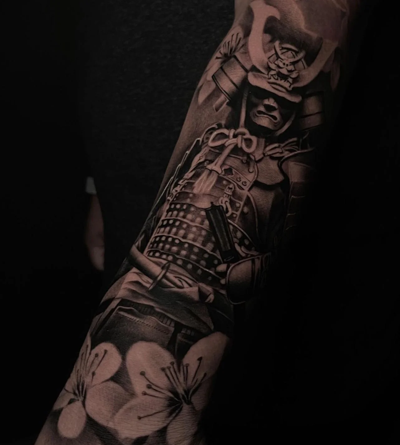 A detailed black and gray tattoo sleeve featuring a warrior in armor and a decorative flower design.