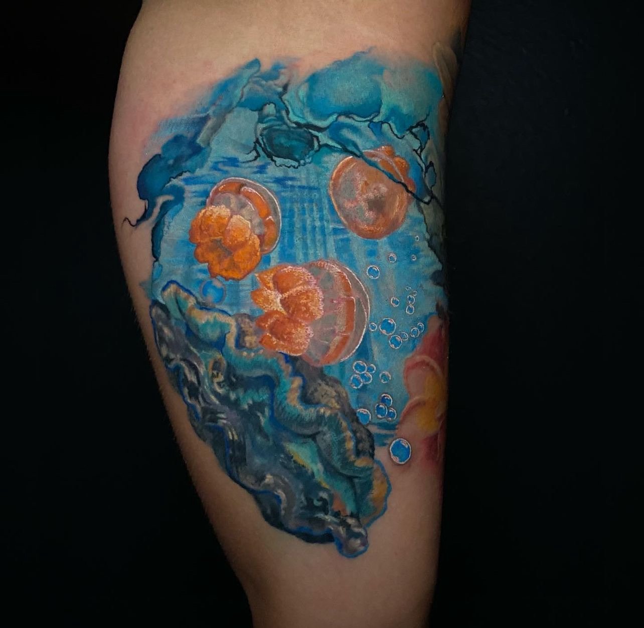 Tattoo of jellyfish underwater scene on person's arm with blue water, coral, and jellyfish.