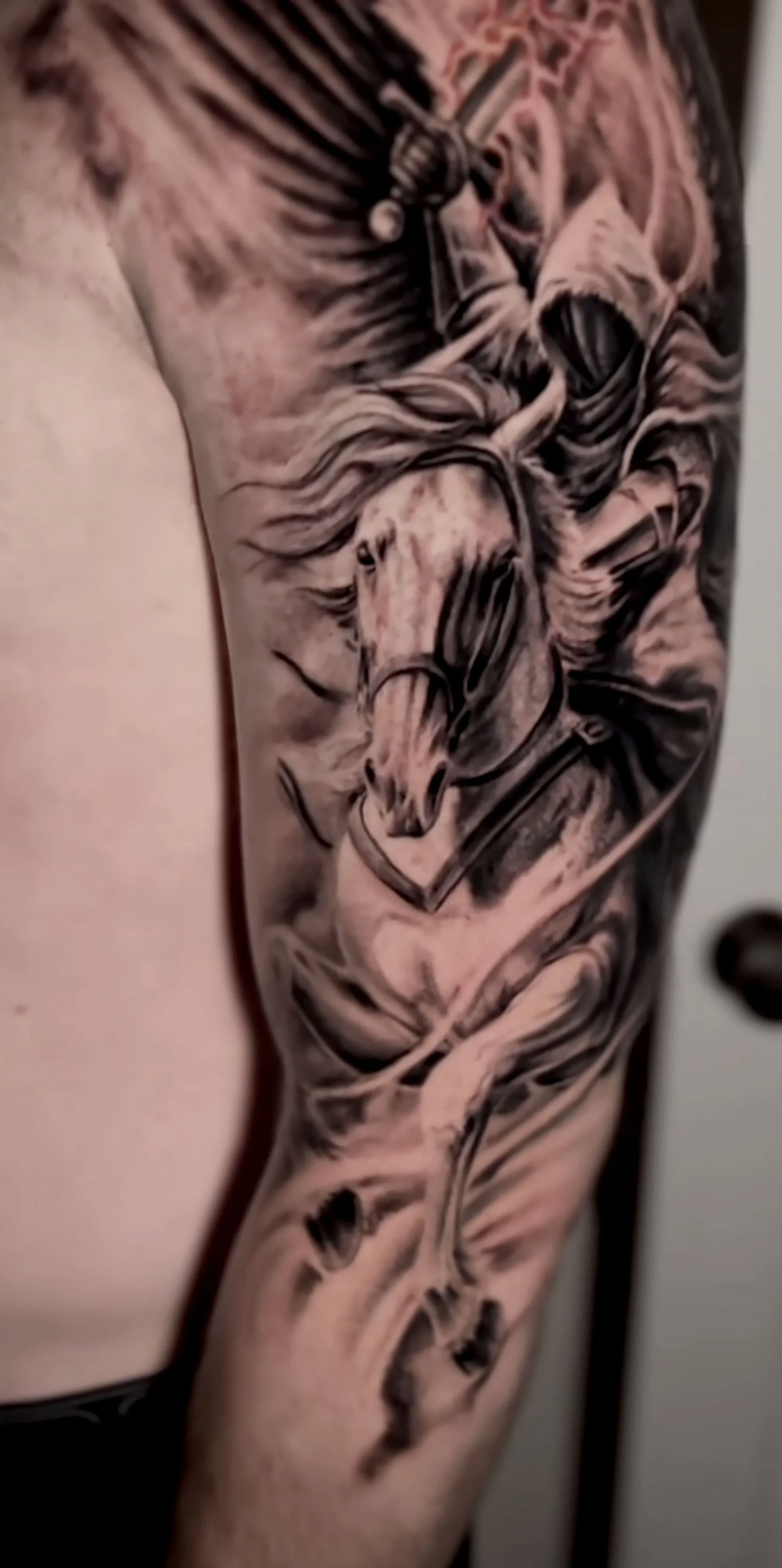 Close-up of a detailed black and gray tattoo of a lion with glasses, a hat, and a microphone on a person's arm.