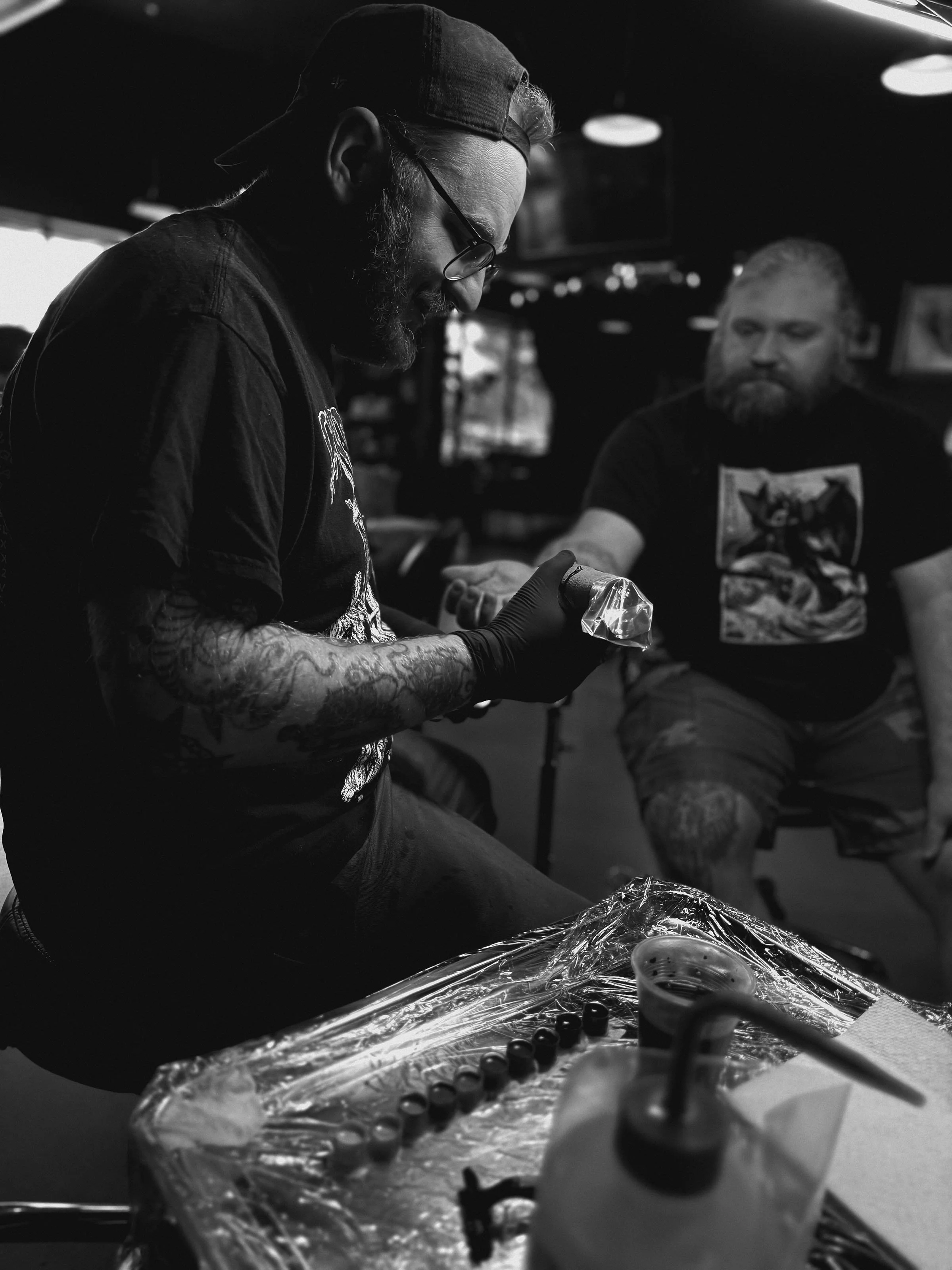 a black and white photo of a tattoo artist working on a clients arm tattoo