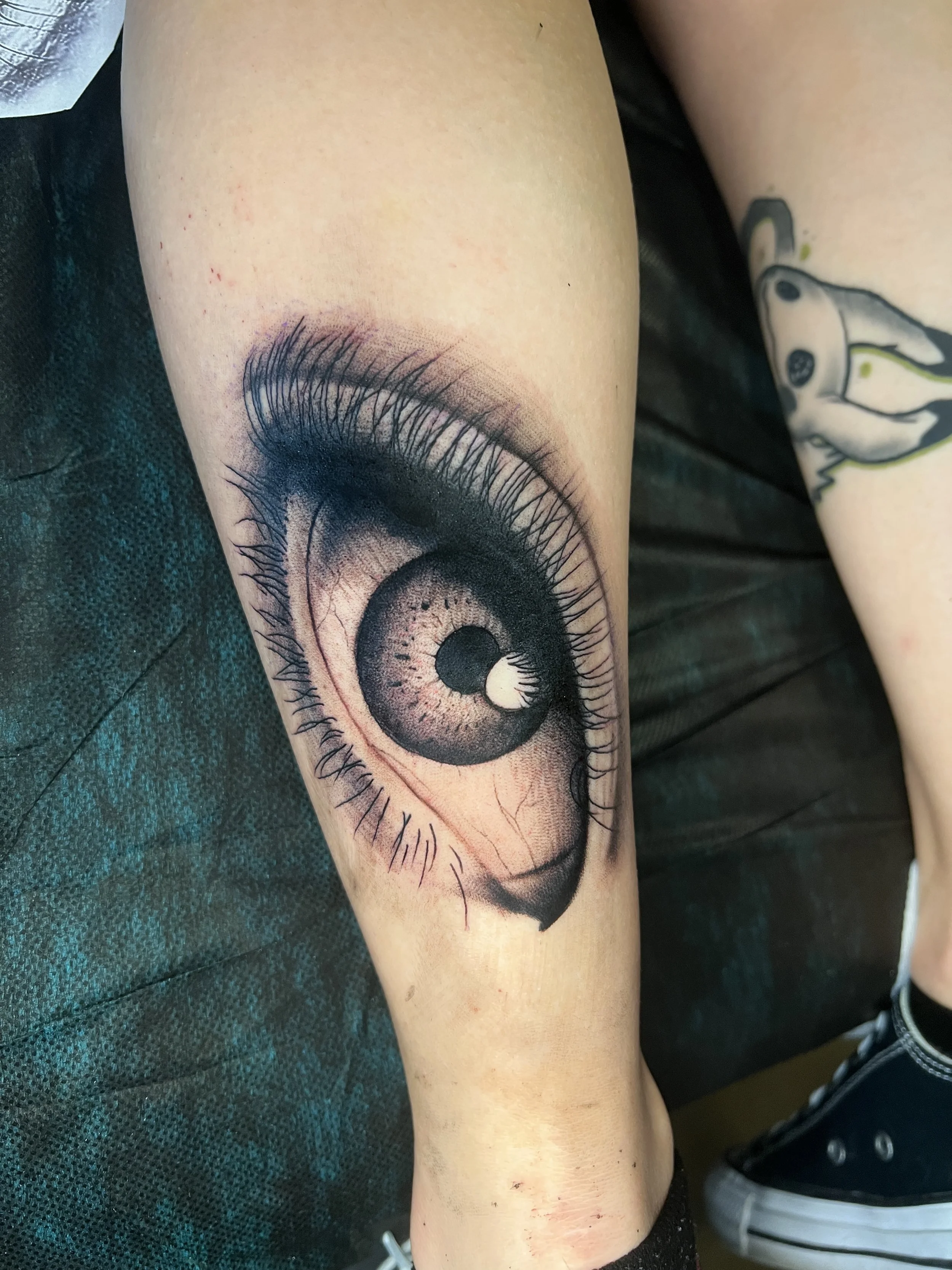 a black and grey realistic tattoo of a woman's eye on the back of a person's calf