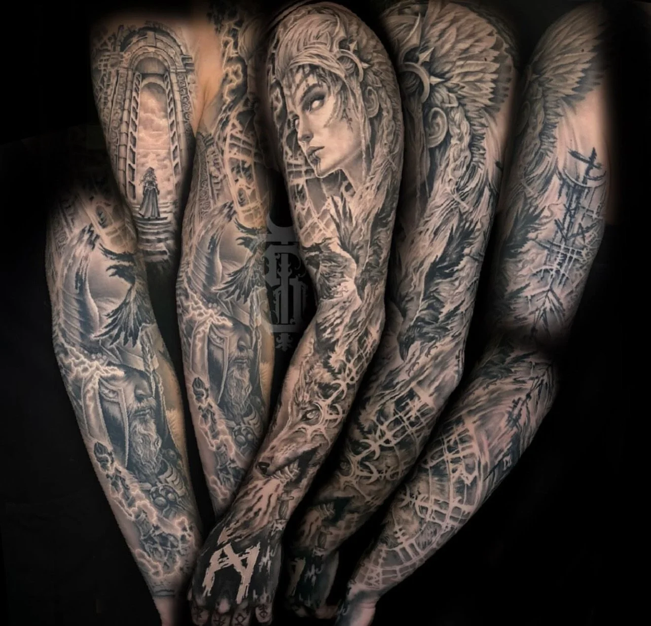 Close-up of multiple black and gray tattoos on person’s arms, featuring a woman’s face, a wolf’s head, and various intricate designs.