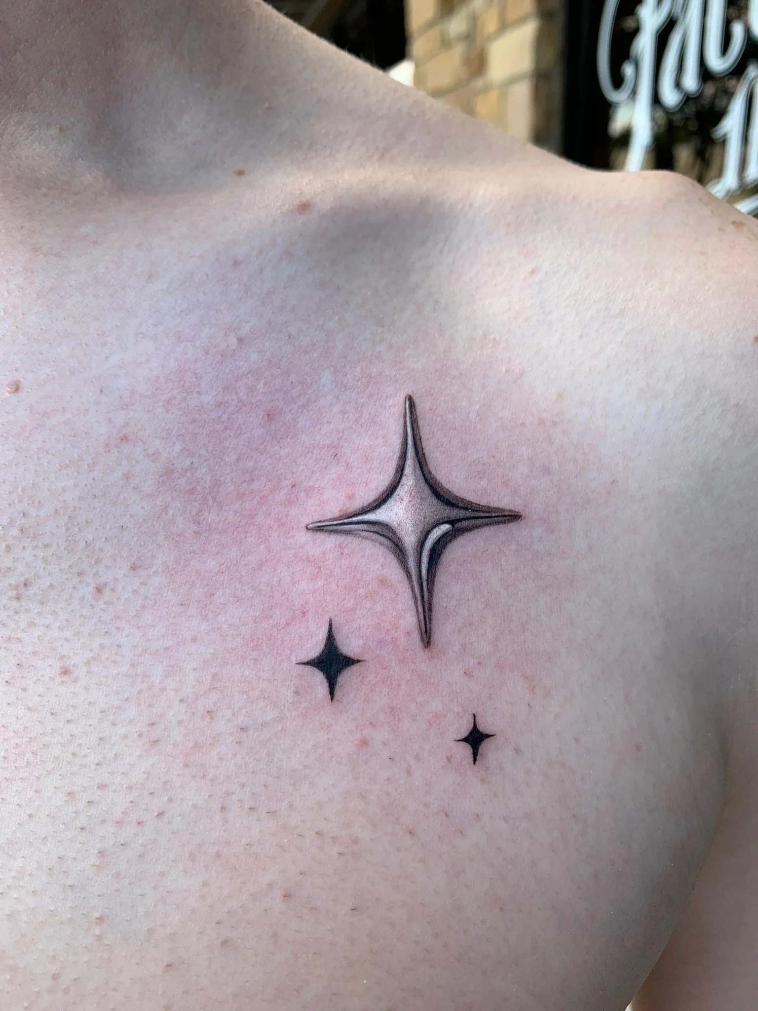 Tattoo of three star-like shapes on person's shoulder, with one larger, detailed star and two smaller solid black stars.