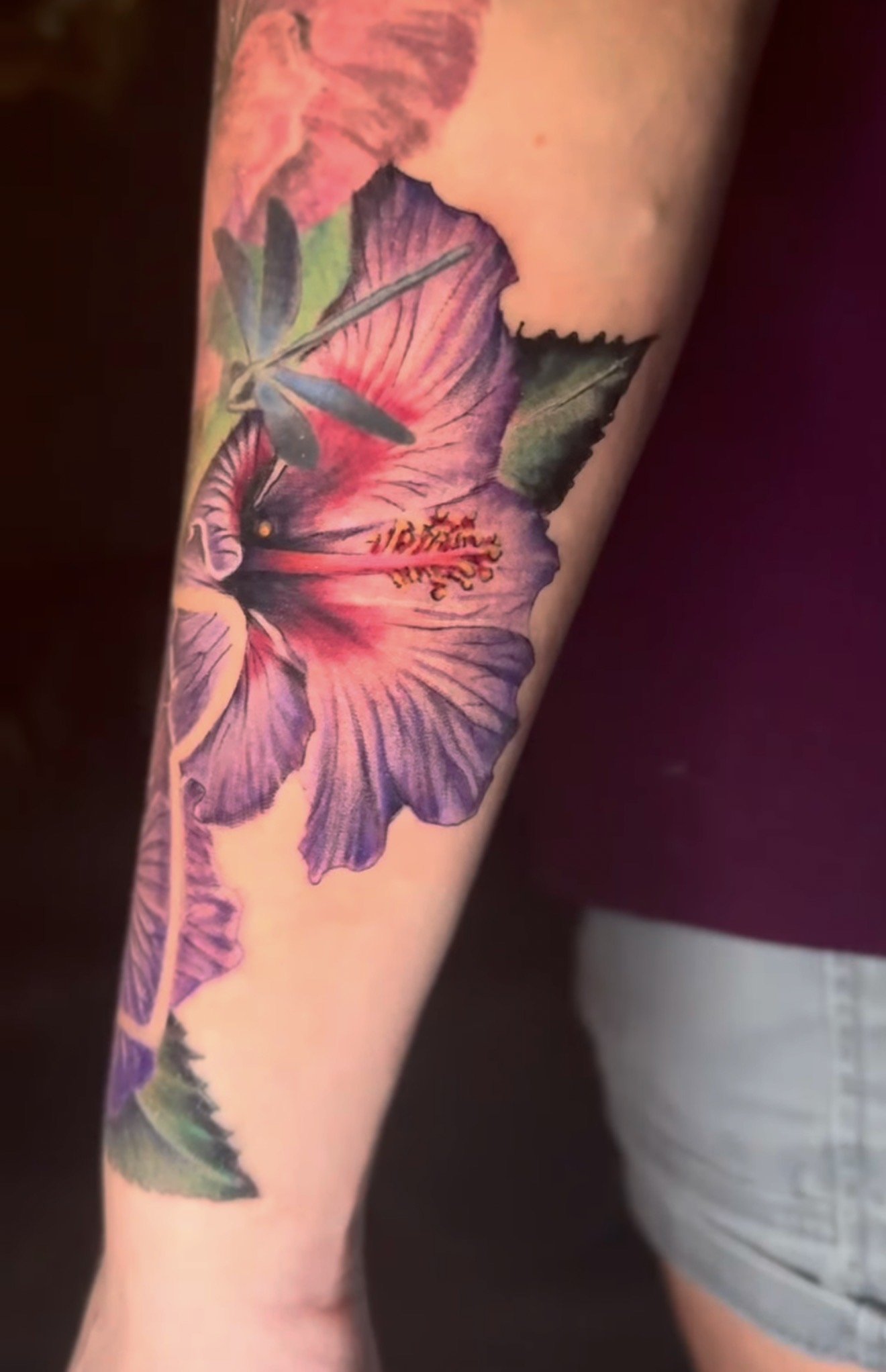 Close-up of a colorful tattoo of a hibiscus flower on a person's arm.
