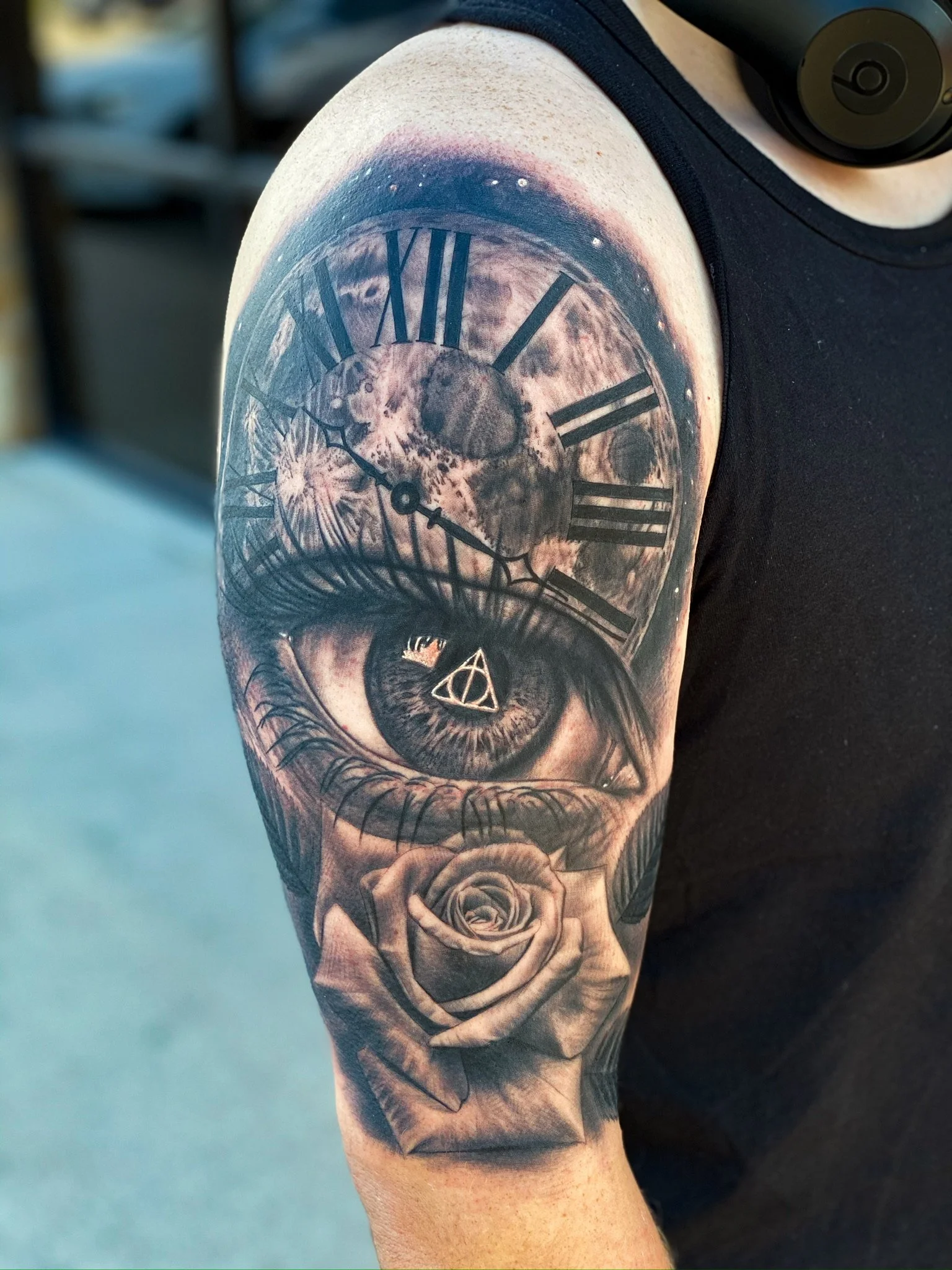 Tattoo of a clock with Roman numerals, a human eye, and a rose on a person's upper arm.