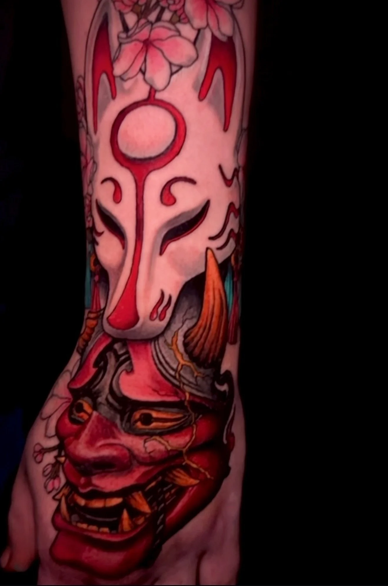 Colorful tattoo on arm featuring a stylized face with bold lines and vibrant colors, including red, pink, orange, and teal.