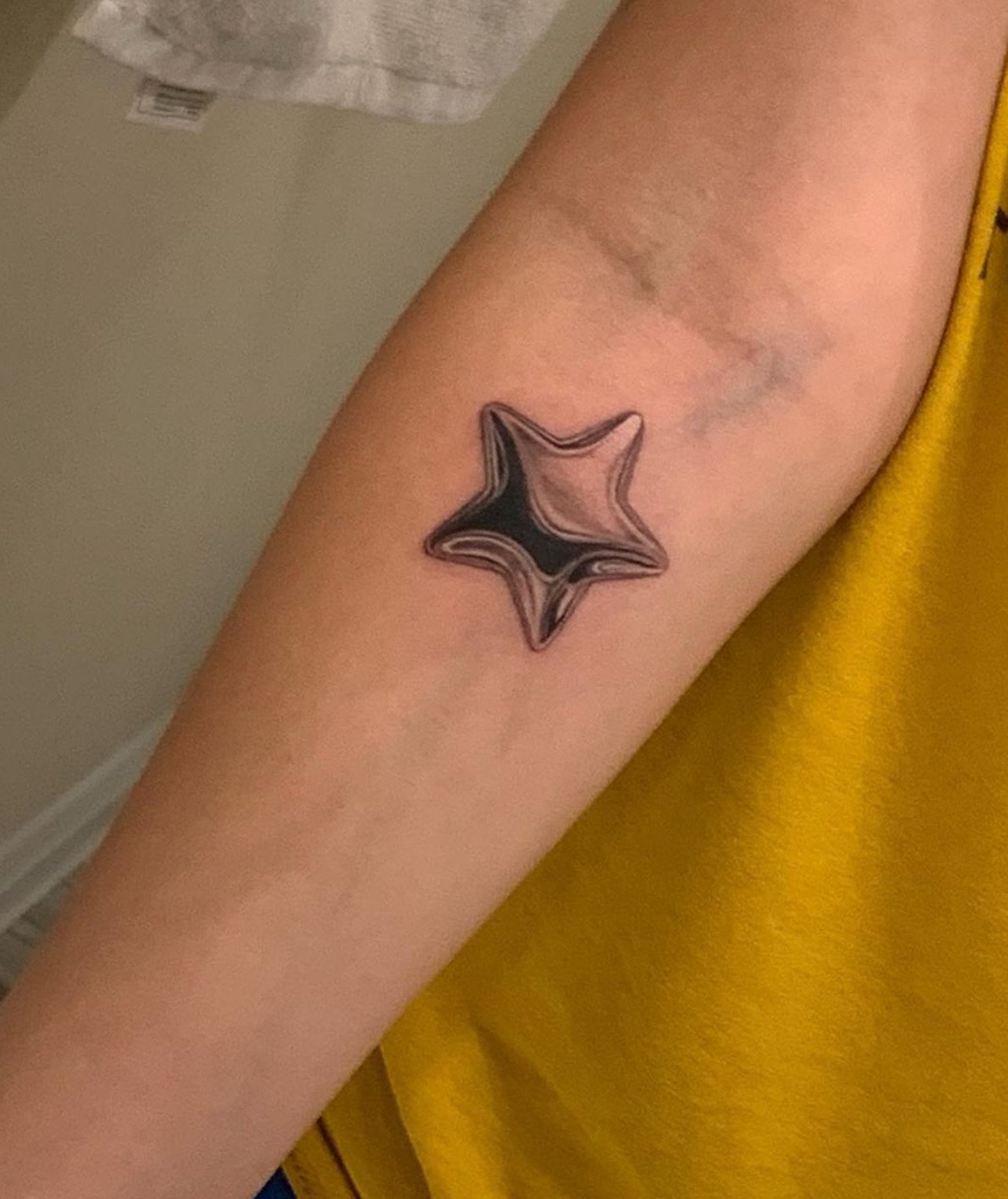 Tattoo of a black and gray star with flowing lines on a person's forearm.