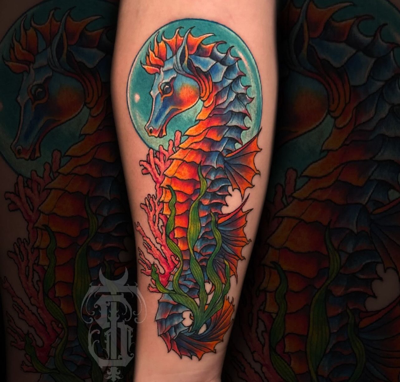 Colorful tattoo of a seahorse with a blue face and orange body, surrounded by coral and seaweed, on a person's arm.