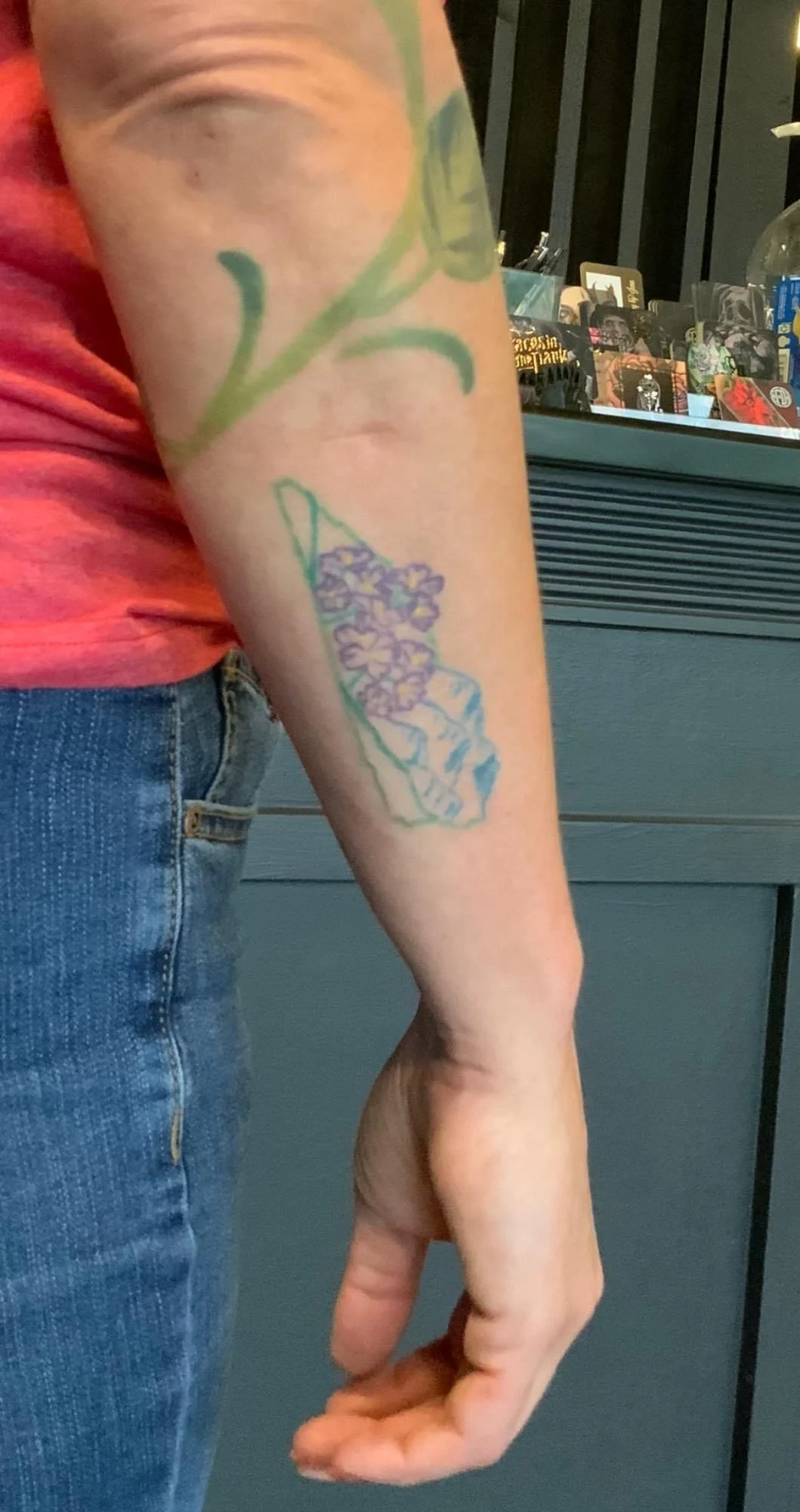 A person's arm with a tattoo of a hand holding purple flowers.