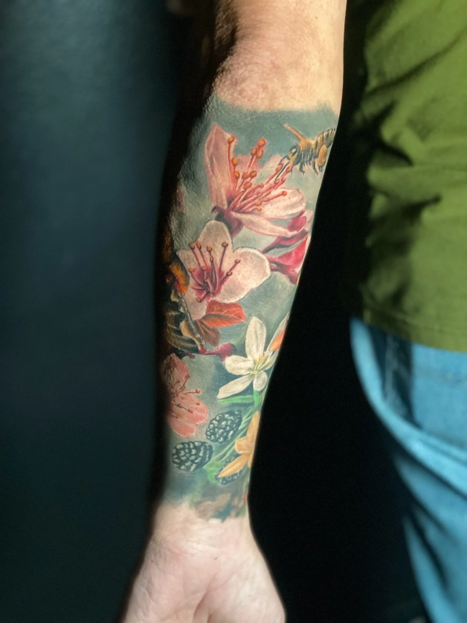 Close-up of a person's arm with a colorful floral tattoo featuring flowers, a bee, and butterflies.