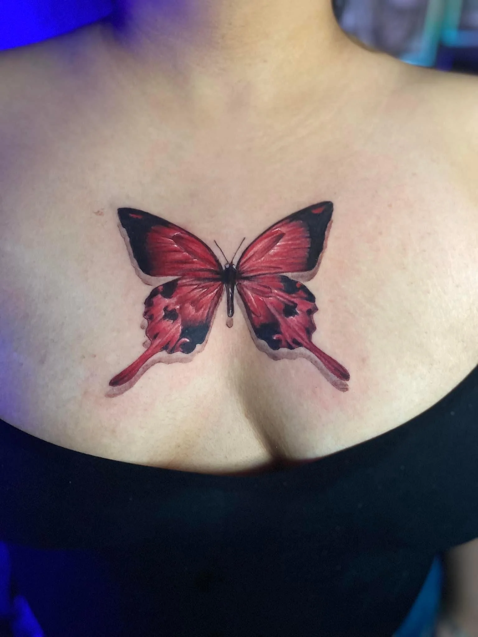 Tattoo of a red butterfly on a person's chest.