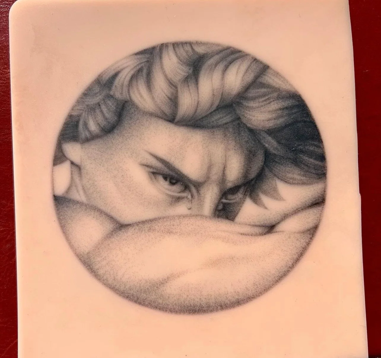 Black and white drawing of a woman with styled hair, partially covering her face with her arm, with a focused and intense expression, within a circular frame.