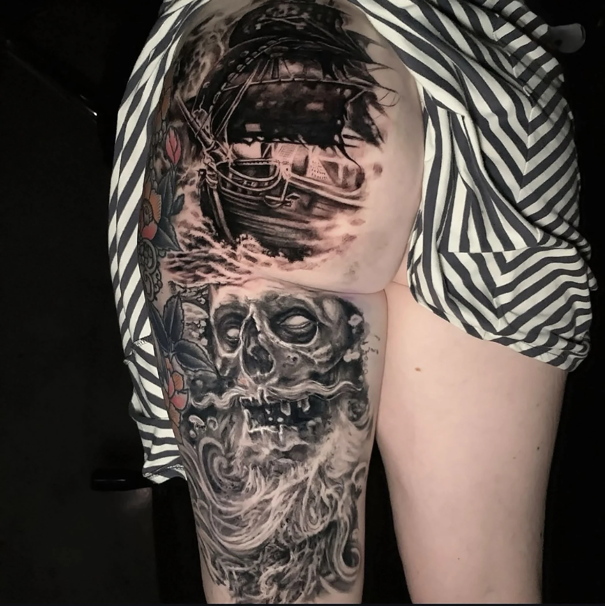 A close-up of a tattoo on a person's arm, depicting a detailed skull with wings, surrounded by intricate patterns.
