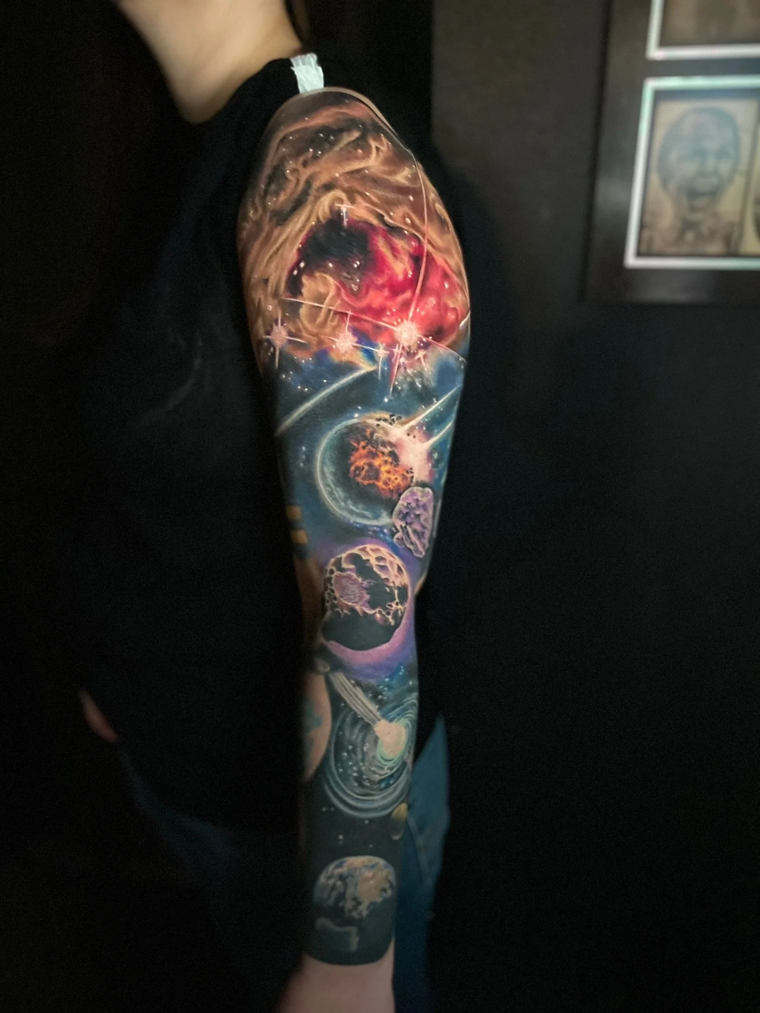 Colorful galaxy-themed tattoo sleeve featuring planets, stars, and cosmic elements on a person's arm.
